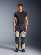 Pantalones laminados Alpinestars Halo Pro Drystar® XF, Mastic Black, pantalones de moto de aventura usados por un modelo con una capa base negra y botas, con paneles beige en los muslos con grandes ventilaciones con cremallera, secciones de rodilla reforzadas en negro y un cinturón con hebilla magnética.