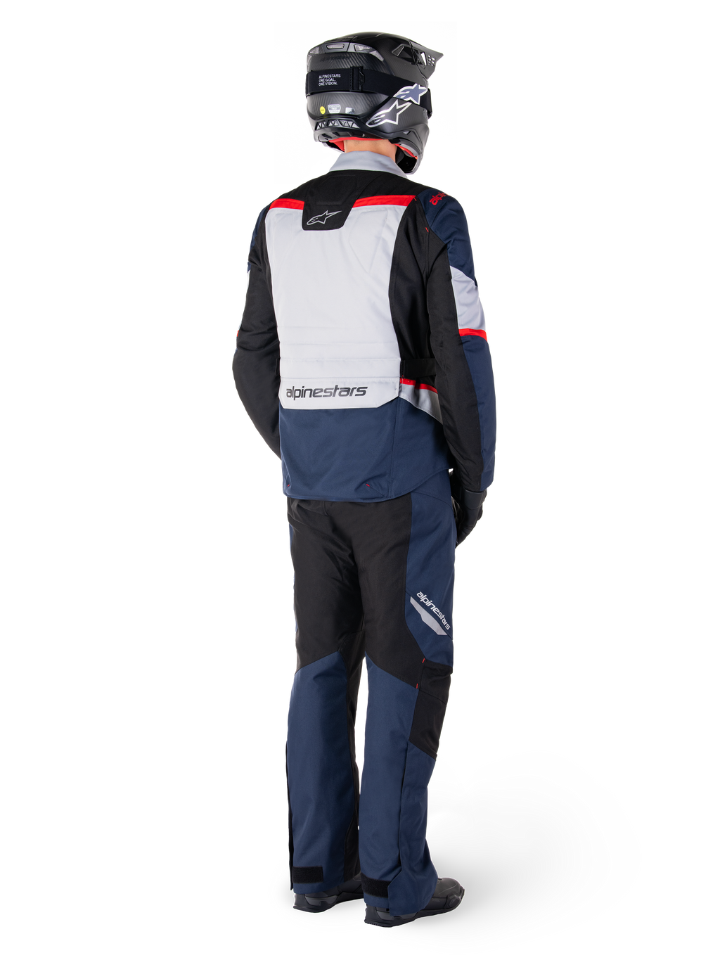 Vista trasera de un motociclista con pantalones Alpinestars ST-1 Waterproof y chaqueta a juego en azul marino, negro y rojo brillante, equipamiento de turismo de aventura con paneles textiles y detalles reflectantes, combinado con casco y botas negras.