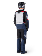 Vista trasera de un motociclista con pantalones Alpinestars ST-1 Waterproof y chaqueta a juego en azul marino, negro y rojo brillante, equipamiento de turismo de aventura con paneles textiles y detalles reflectantes, combinado con casco y botas negras.