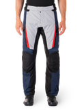 Pantalones Alpinestars ST-1 Waterproof, pantalones de turismo para moto, azul oscuro y gris claro con detalles en rojo brillante, paneles negros reforzados en las rodillas, vista frontal con botas negras, equipamiento de turismo de aventura impermeable