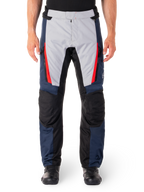 Pantalones Alpinestars ST-1 Waterproof, pantalones de turismo para moto, azul oscuro y gris claro con detalles en rojo brillante, paneles negros reforzados en las rodillas, vista frontal con botas negras, equipamiento de turismo de aventura impermeable