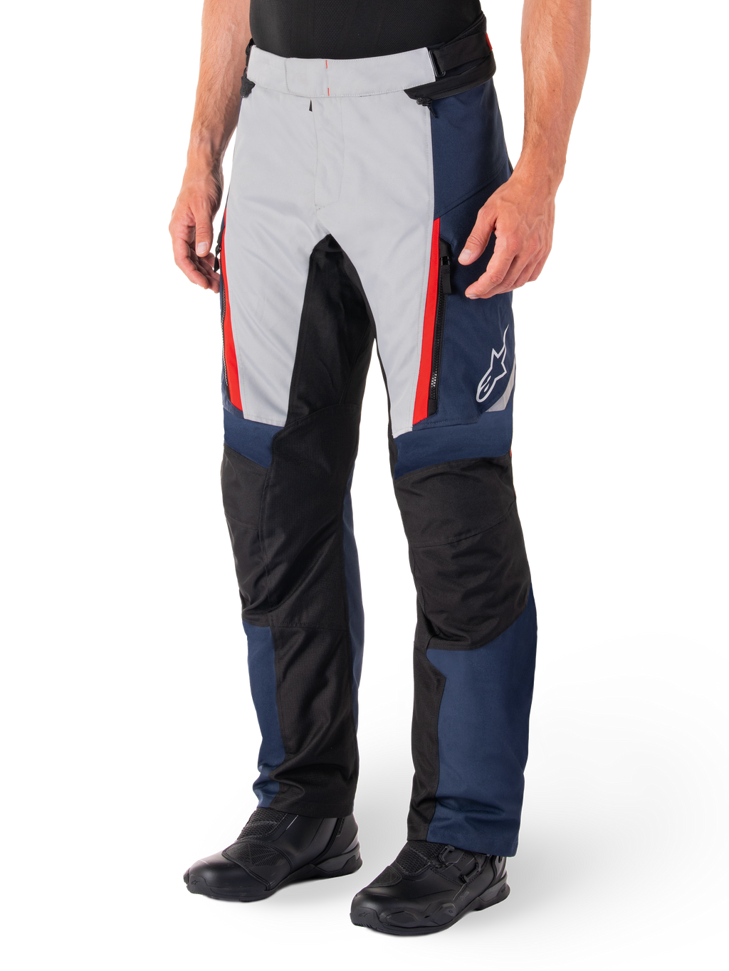 Pantalones Alpinestars St-1 Waterproof, pantalones de touring para moto, azul oscuro, negro y rojo brillante, con paneles frontales gris claro, acentos de cremalleras rojas, secciones de rodilla reforzadas en negro y logo blanco de Alpinestars en el lateral, usados con botas de moto negras