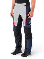 Pantalones Alpinestars St-1 Waterproof, pantalones de touring para moto, azul oscuro, negro y rojo brillante, con paneles frontales gris claro, acentos de cremalleras rojas, secciones de rodilla reforzadas en negro y logo blanco de Alpinestars en el lateral, usados con botas de moto negras