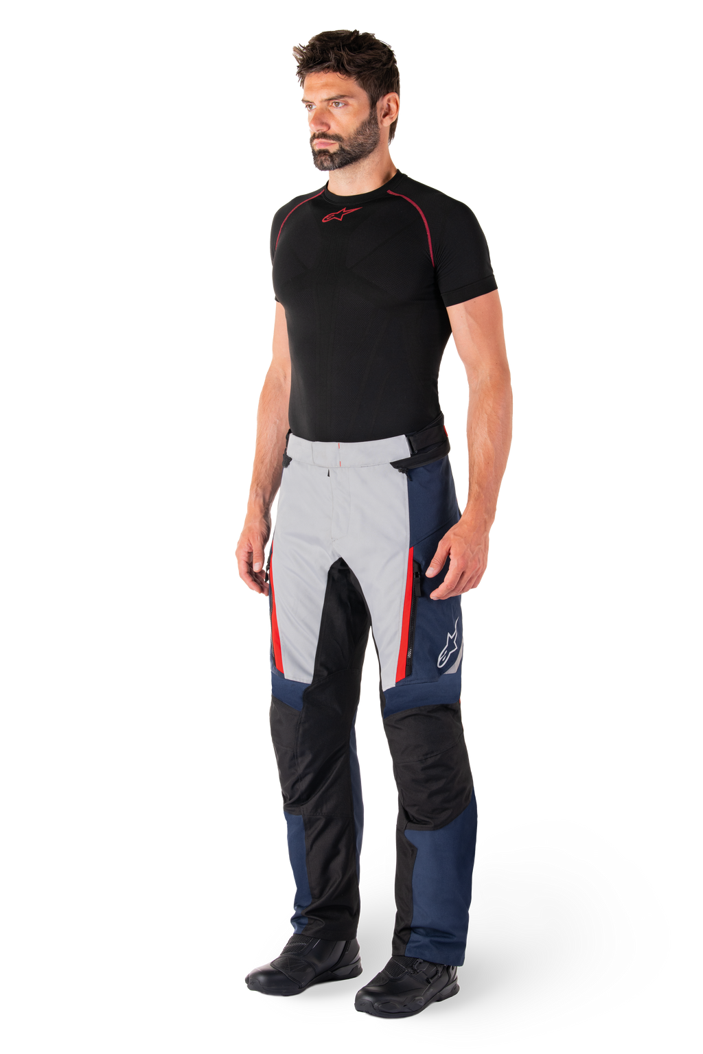 Pantalones Alpinestars St-1 Waterproof, pantalones de moto para turismo, azul oscuro, negro y rojo brillante, usados por un modelo con capa base negra y botas negras, incluye bolsillos con cremallera y el logotipo de Alpinestars en la pierna