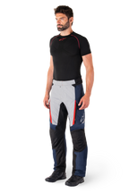 Pantalones Alpinestars St-1 Waterproof, pantalones de moto para turismo, azul oscuro, negro y rojo brillante, usados por un modelo con capa base negra y botas negras, incluye bolsillos con cremallera y el logotipo de Alpinestars en la pierna