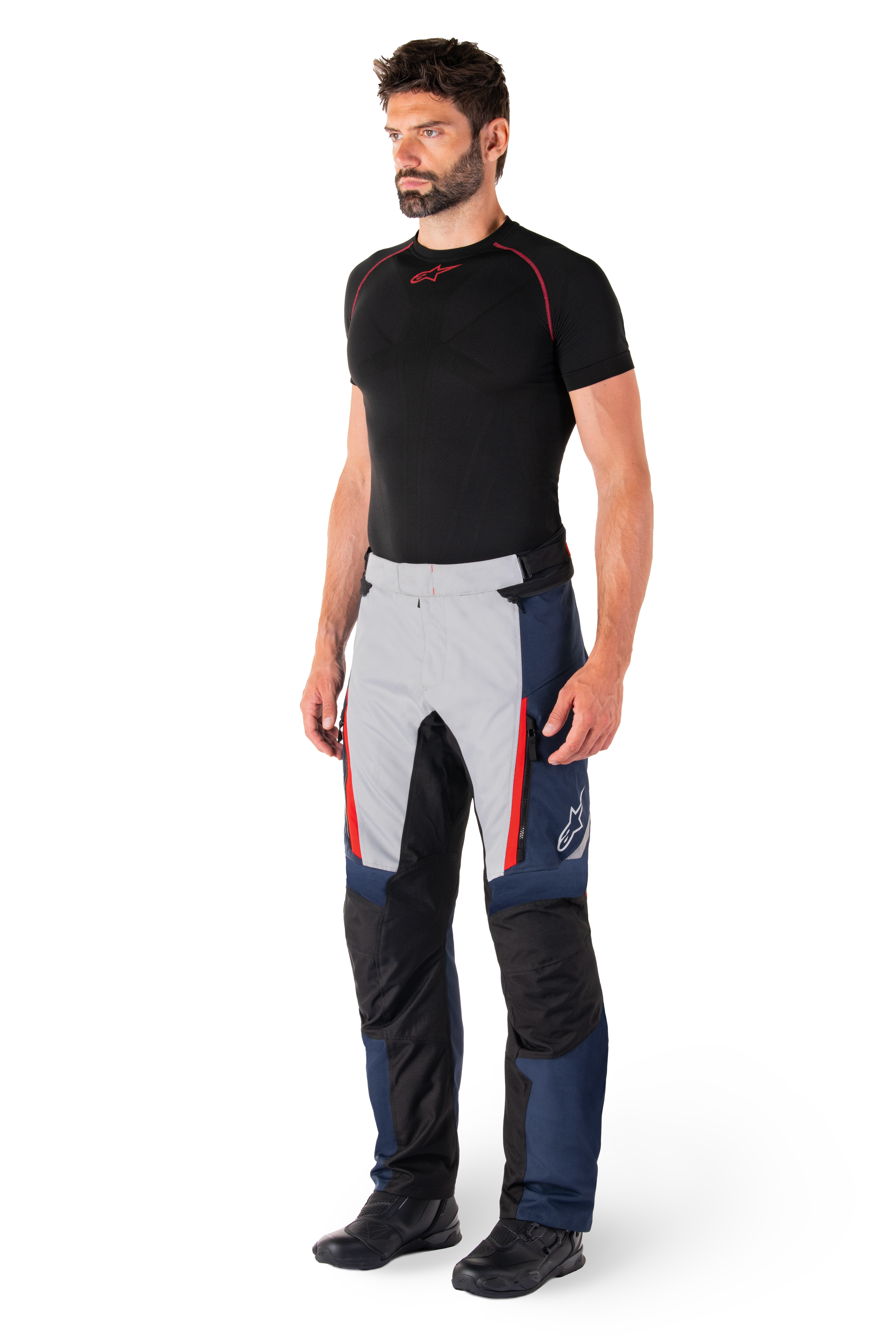 Pantalones Alpinestars St-1 Waterproof, pantalones de moto para turismo, azul oscuro, negro y rojo brillante, usados por un modelo con capa base negra y botas negras, incluye bolsillos con cremallera y el logotipo de Alpinestars en la pierna