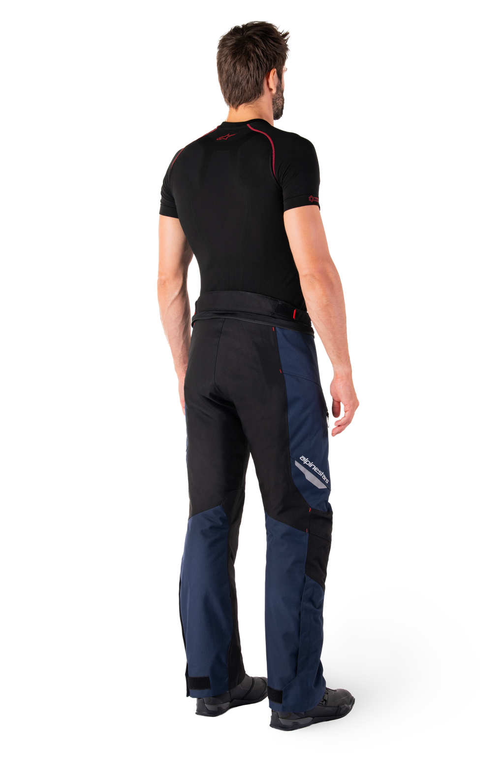 Alpinestars St-1 Waterproof Pants, pantalones de turismo de aventura, azul oscuro, negro y rojo brillante, vista lateral trasera usados con una capa base negra de manga corta y botas de conducción negras, con diseño aerodinámico, logotipos reflectantes y acentos rojos