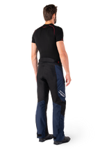 Alpinestars St-1 Waterproof Pants, pantalones de turismo de aventura, azul oscuro, negro y rojo brillante, vista lateral trasera usados con una capa base negra de manga corta y botas de conducción negras, con diseño aerodinámico, logotipos reflectantes y acentos rojos