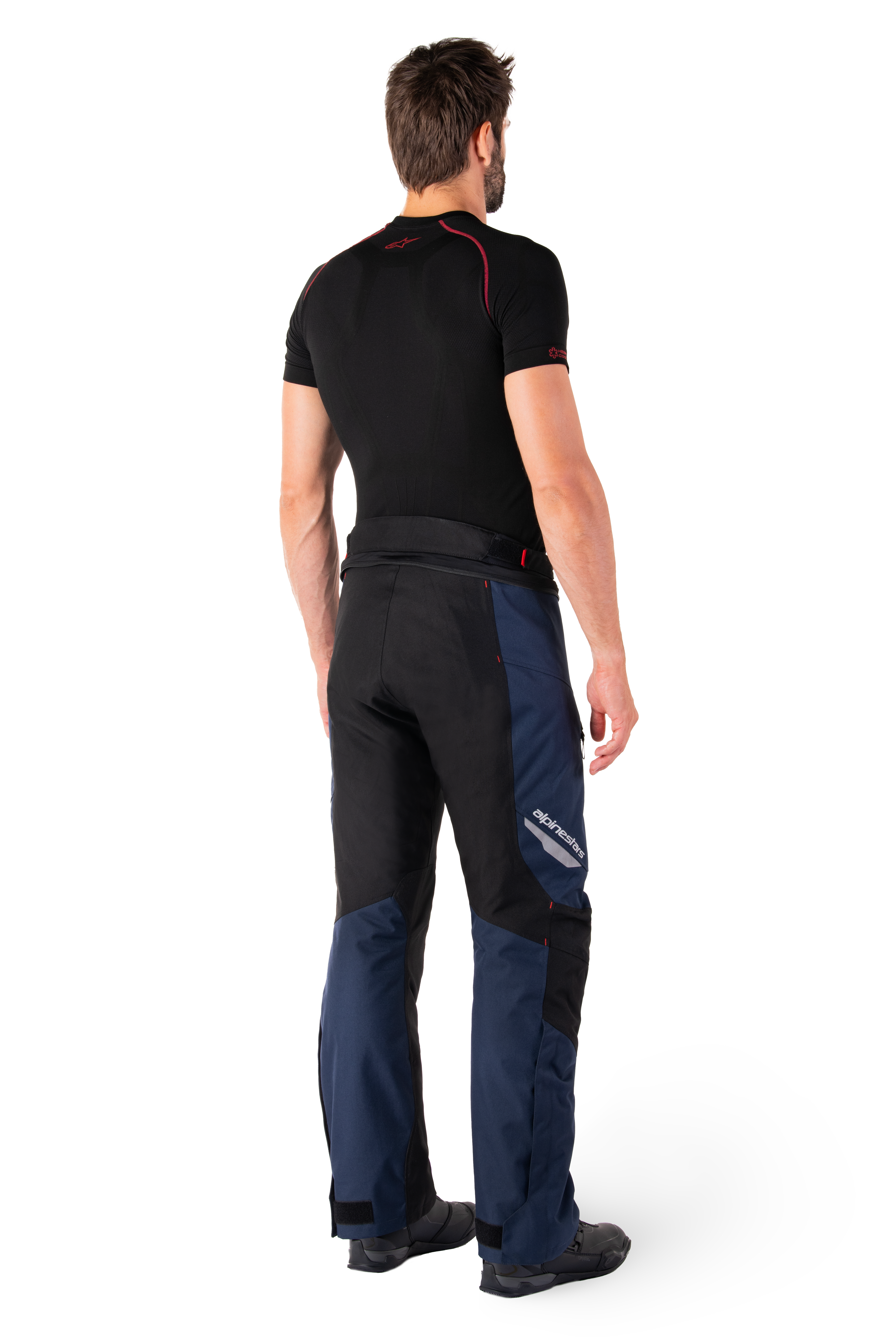 Alpinestars St-1 Waterproof Pants, pantalones de turismo de aventura, azul oscuro, negro y rojo brillante, vista lateral trasera usados con una capa base negra de manga corta y botas de conducción negras, con diseño aerodinámico, logotipos reflectantes y acentos rojos