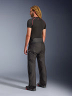 Pantalones Alpinestars Andes V4 Drystar® - Long, pantalones de moto de aventura, negros, vista trasera de tres cuartos en modelo, diseño textil duradero con paneles reforzados en el asiento y las rodillas, con el logotipo de la estrella de Alpinestars, usados con una capa base negra y botas de moto