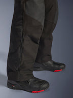 Alpinestars Andes V4 Drystar® Pants - Long, pantalones negros de aventura para motocicleta, primer plano de la parte inferior de la pierna mostrando el puño con cremallera ajustable y construcción textil duradera, usados con botas de moto negras con detalles rojos