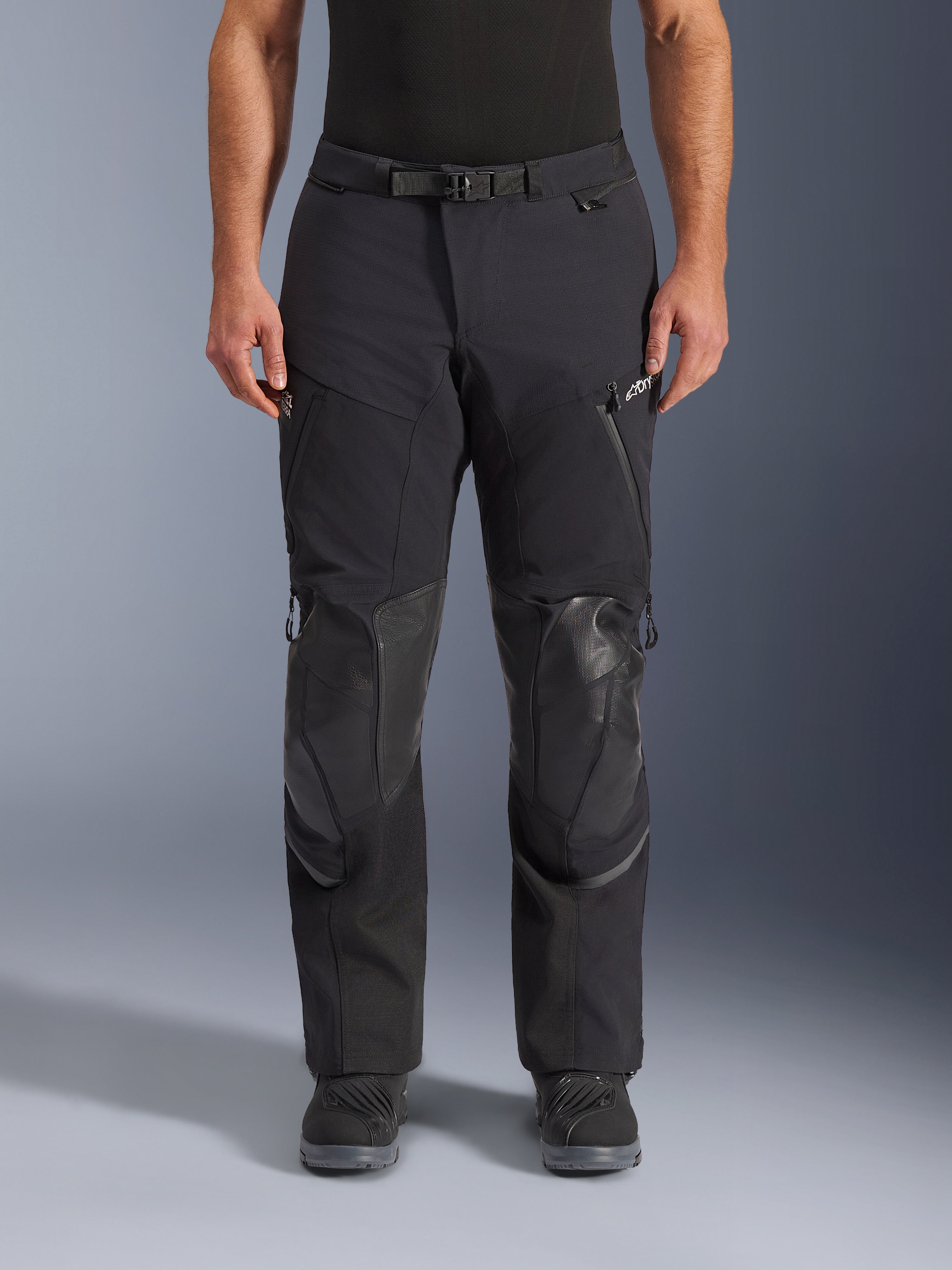 Alpinestars Andes Pro Drystar® XF Pants, pantalones de motociclismo adventure touring en Negro Gris Oscuro, vista frontal, con construcción laminada de 3 capas, paneles de protección integrados en las rodillas, bolsillos con cremallera impermeables y hebilla magnética en la cintura, combinados con botas de conducción negras.