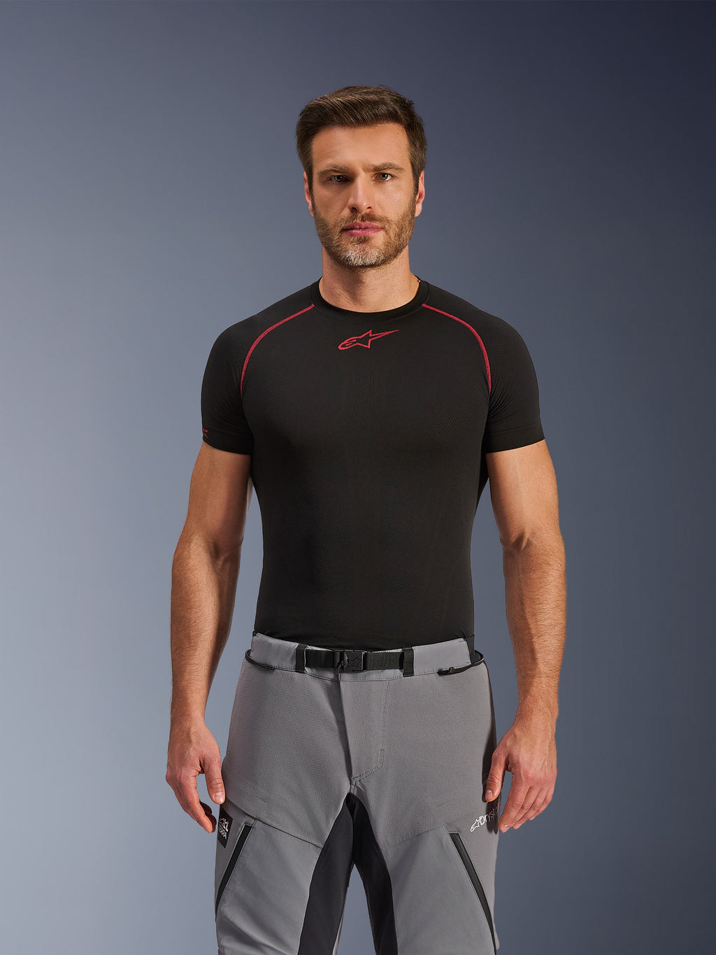 Pantalones Alpinestars Andes Pro Drystar® XF, pantalones de motociclismo de aventura, gris oscuro y negro, lucidos por un modelo masculino con una capa base técnica negra, con cintura con hebilla magnética, construcción textil duradera y marca Drystar® XF para touring en cualquier clima.