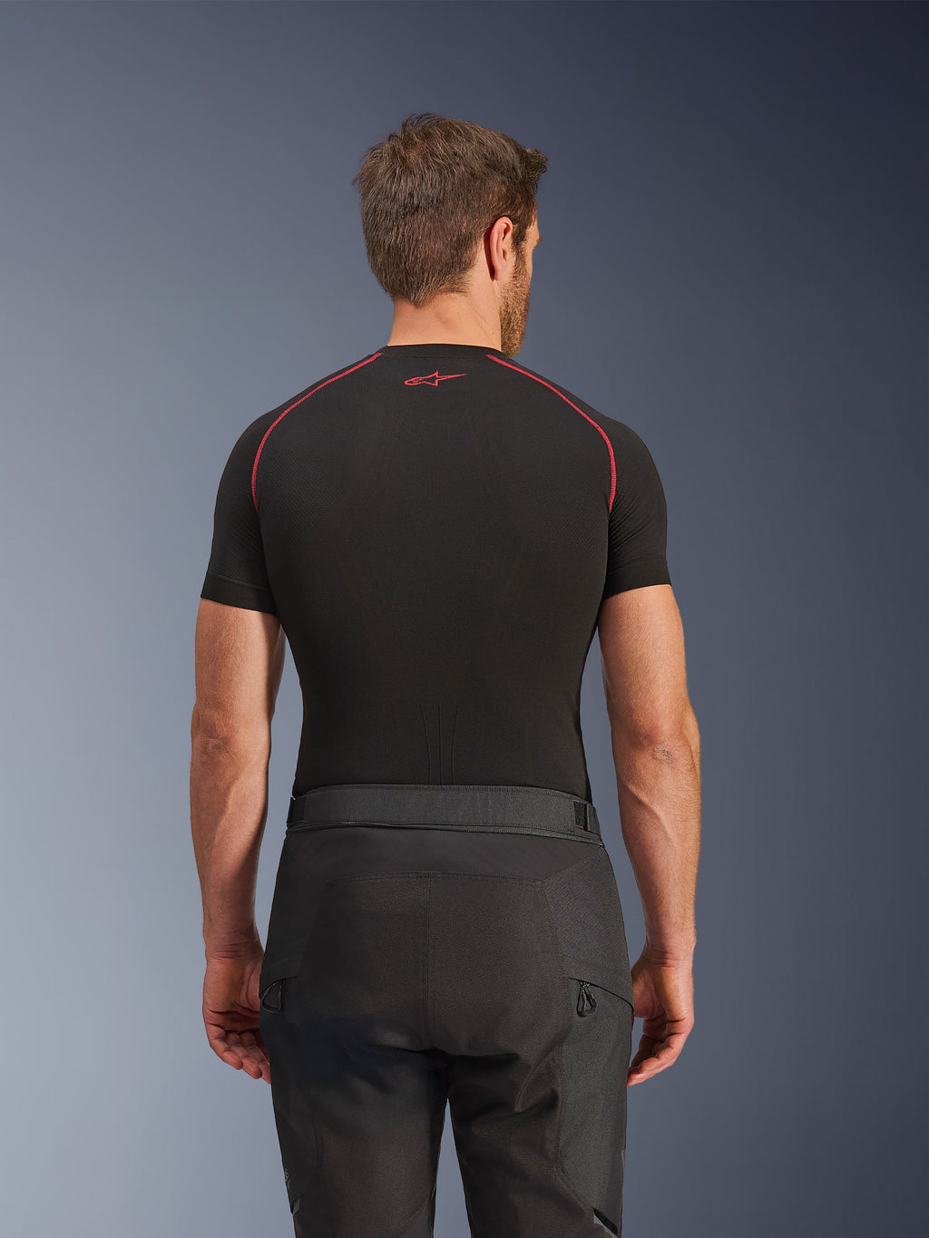 Pantalones Alpinestars Cusco Drystar®, pantalones de moto negros, vista trasera de un piloto con equipamiento adventure touring, camiseta de compresión negra de manga corta con costuras rojas, construcción duradera en tejido ripstop y 600D.