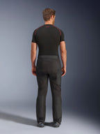 Motociclista con pantalones Alpinestars Cusco Drystar®, pantalones de motociclismo adventure negros, vista trasera, combinados con una camiseta de compresión negra de manga corta y botas de motociclismo negras, con un diseño textil duradero y paneles articulados para touring