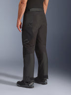 Pantalones Alpinestars Cusco Drystar®, pantalones de moto, negro, vista trasera de tres cuartos que muestra el bolsillo con cremallera en el muslo y paneles articulados, combinados con botas de moto negras, diseño duradero de adventure touring con logotipos sutiles