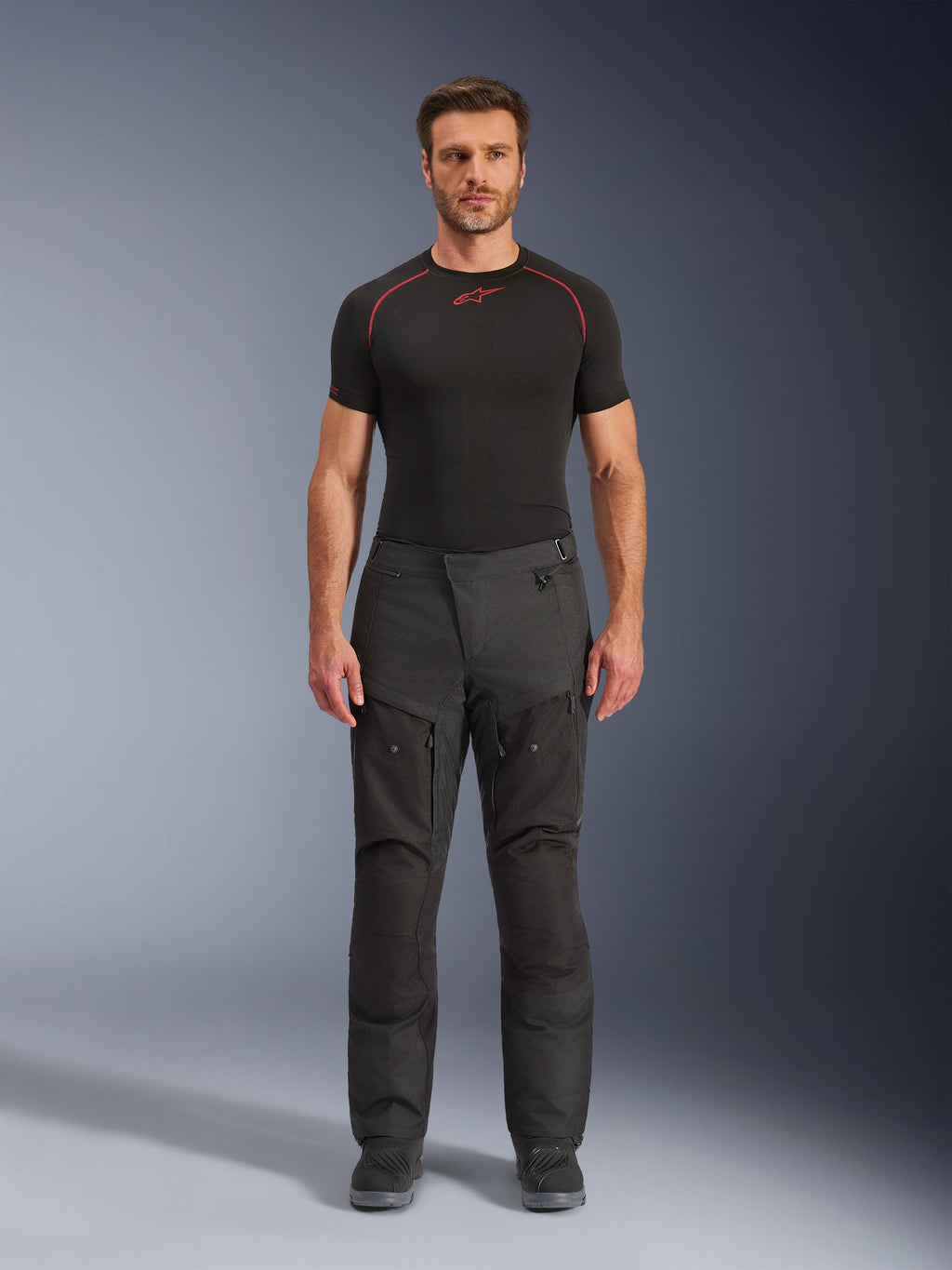 Pantalones Alpinestars Cusco Drystar®, pantalones textiles de moto, negros, usados por un modelo con una capa base negra y botas, diseño adventure touring con paneles de ventilación con cremallera en los muslos y construcción duradera de múltiples paneles.