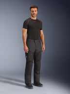 Pantalones Alpinestars Cusco Drystar®, pantalones de moto textiles negros, usados por un modelo con una capa base negra y botas, con tejido ripstop, bolsillos cargo grandes con la marca 'Terra' y diseño ergonómico para conducción de aventura.