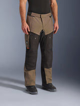 Pantalones Alpinestars Cusco Drystar®, pantalones de motociclismo adventure, color Walnut Black, mostrados en un modelo con botas negras, con un diseño de múltiples paneles en marrón y negro, bolsillos con cremallera y rodillas reforzadas para touring