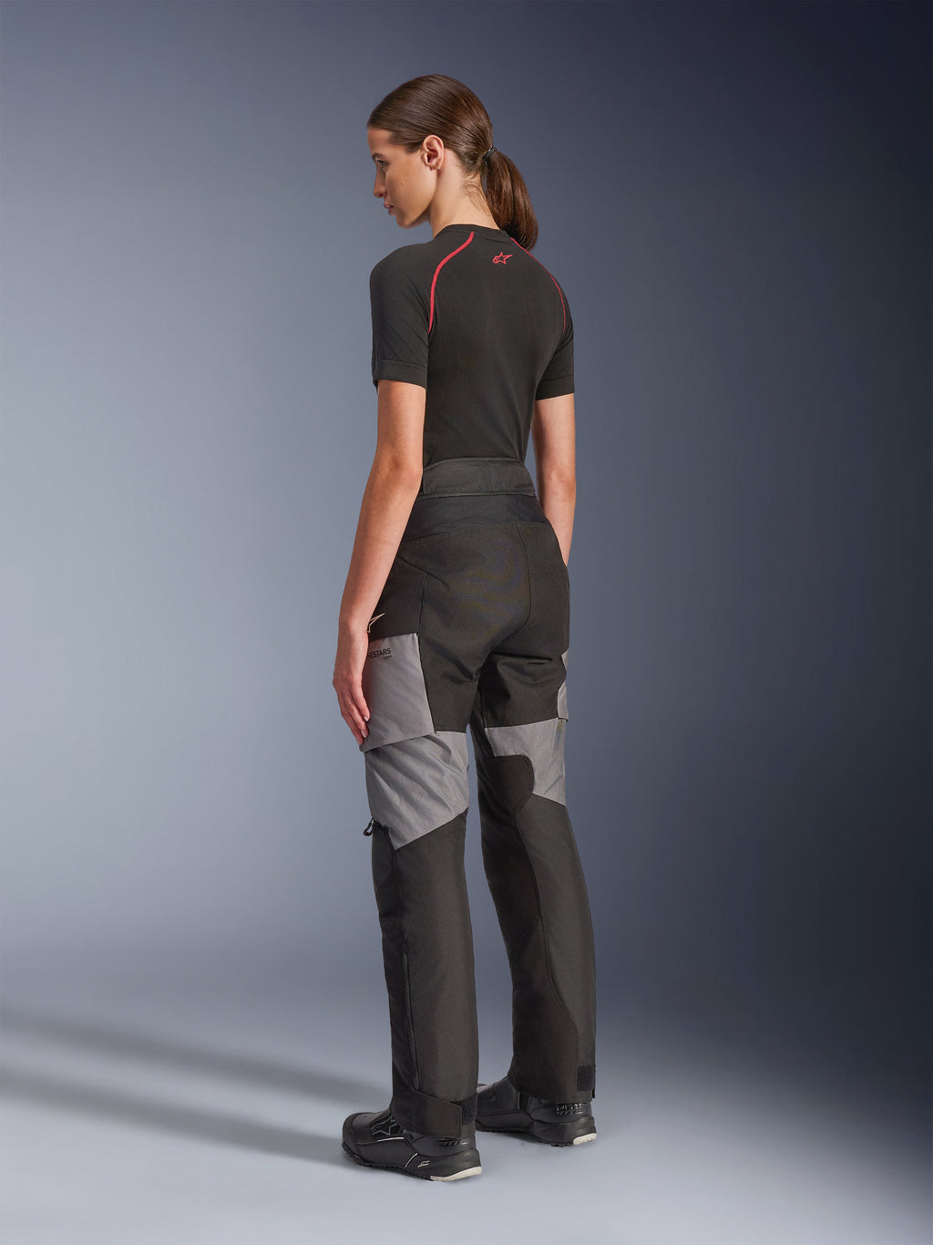 Pantalones Stella Andes V4 Drystar® para mujer, pantalones de moto para aventura y turismo en negro y gris oscuro, vista trasera y lateral en modelo, con construcción textil duradera con paneles de refuerzo grises y un ajuste entallado para motociclistas