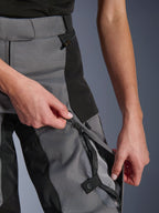 Pantalones Alpinestars Stella Andes V4 Drystar® para mujer, negro y gris oscuro, primer plano de manos abriendo la ventilación con cremallera en el muslo para mostrar la malla transpirable, cremalleras impermeables, construcción textil duradera para conducción de aventura
