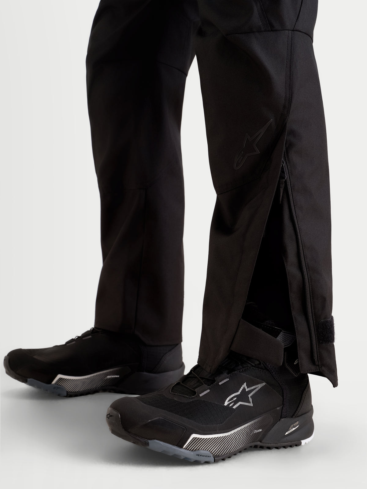 Alpinestars Stella C-1 Waterproof Pantalones, pantalones de moto urbanos para mujer, negros, vista en primer plano de aberturas extendidas en la parte inferior de las piernas con fuelles con cremallera sobre calzado de moto