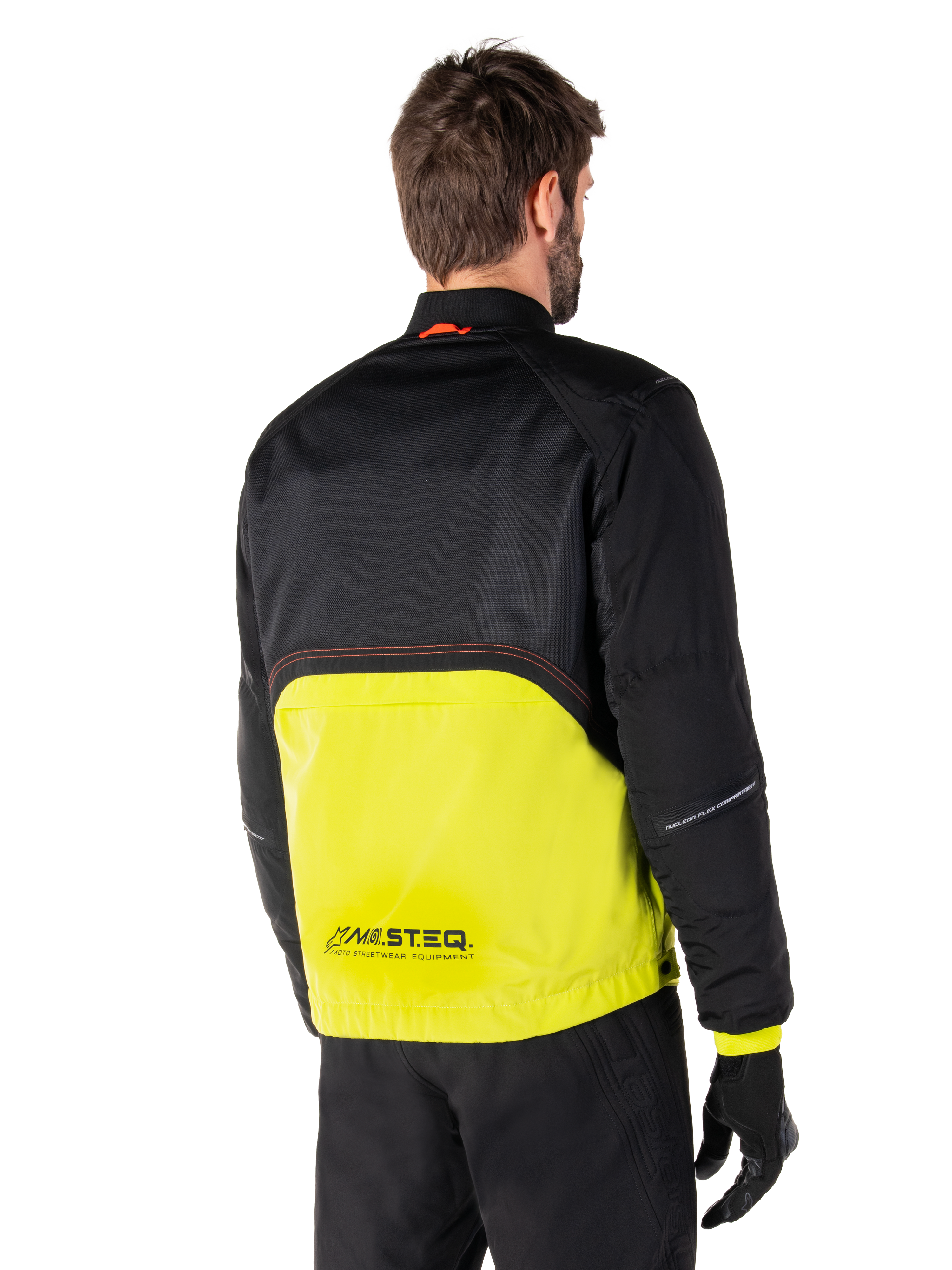 Alpinestars Mootant Waterproof Parka, chaqueta de moto, Lime Punch y negro, vista trasera que muestra la malla superior negra y la sección inferior verde lima brillante, con la marca MO.ST.EQ., usada con pantalones de conducción y guantes negros