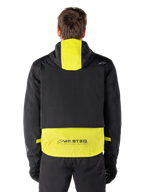 Parka impermeable Alpinestars Mootant, chaqueta de moto, en Lime Punch y negro, vista trasera que muestra el diseño con capucha y la marca reflectante MO.ST.EQ. en la parte inferior de la espalda, combinada con pantalones y guantes de moto negros.