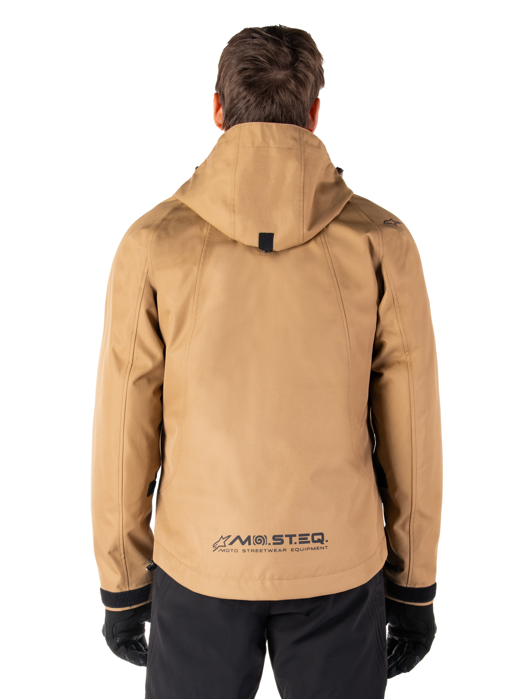 Parka impermeable Alpinestars Morush, color marrón Utility Brown, vista trasera, con capucha y logotipo MO.ST.EQ. en la parte inferior de la espalda, combinada con pantalones y guantes negros, equipamiento de motociclismo de estilo urbano moderno