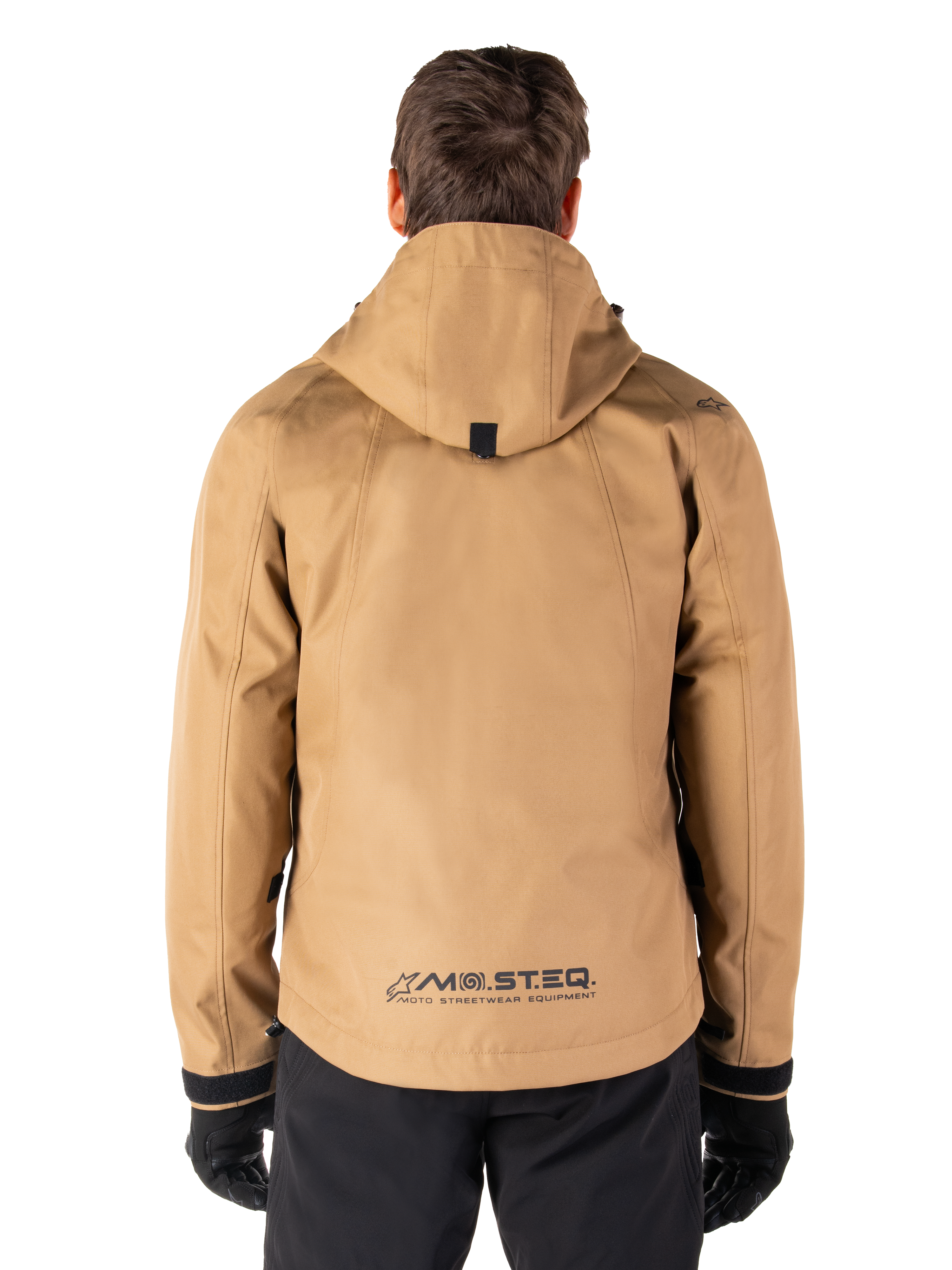 Parka impermeable Alpinestars Morush, color marrón Utility Brown, vista trasera, con capucha y logotipo MO.ST.EQ. en la parte inferior de la espalda, combinada con pantalones y guantes negros, equipamiento de motociclismo de estilo urbano moderno