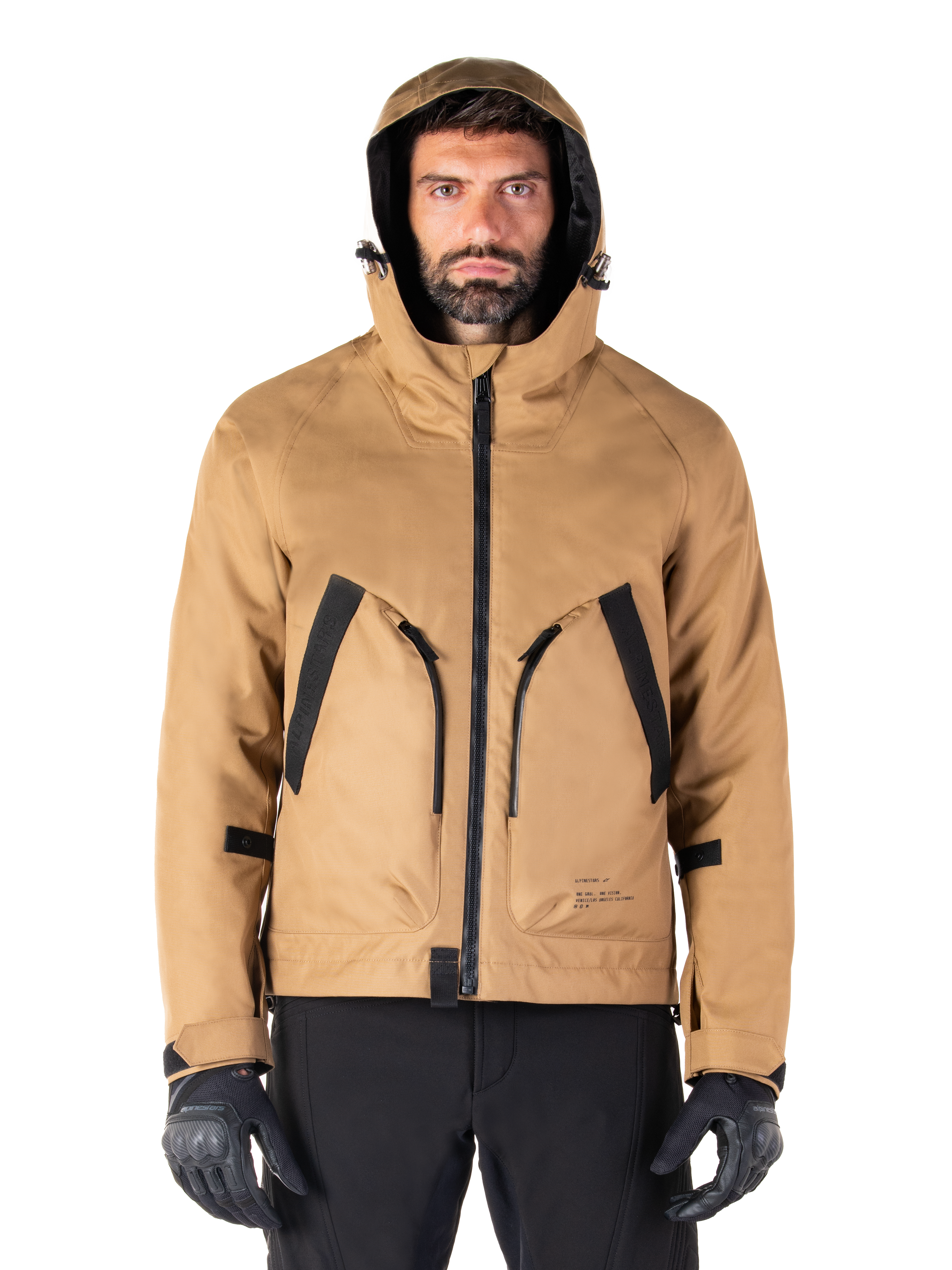 Parka impermeable Alpinestars Morush, chaqueta de moto, marrón utility, diseño con capucha inspirado en el estilo urbano con grandes bolsillos delanteros con detalles en negro, usada con guantes y pantalones de moto negros, equipamiento de moto urbano contemporáneo