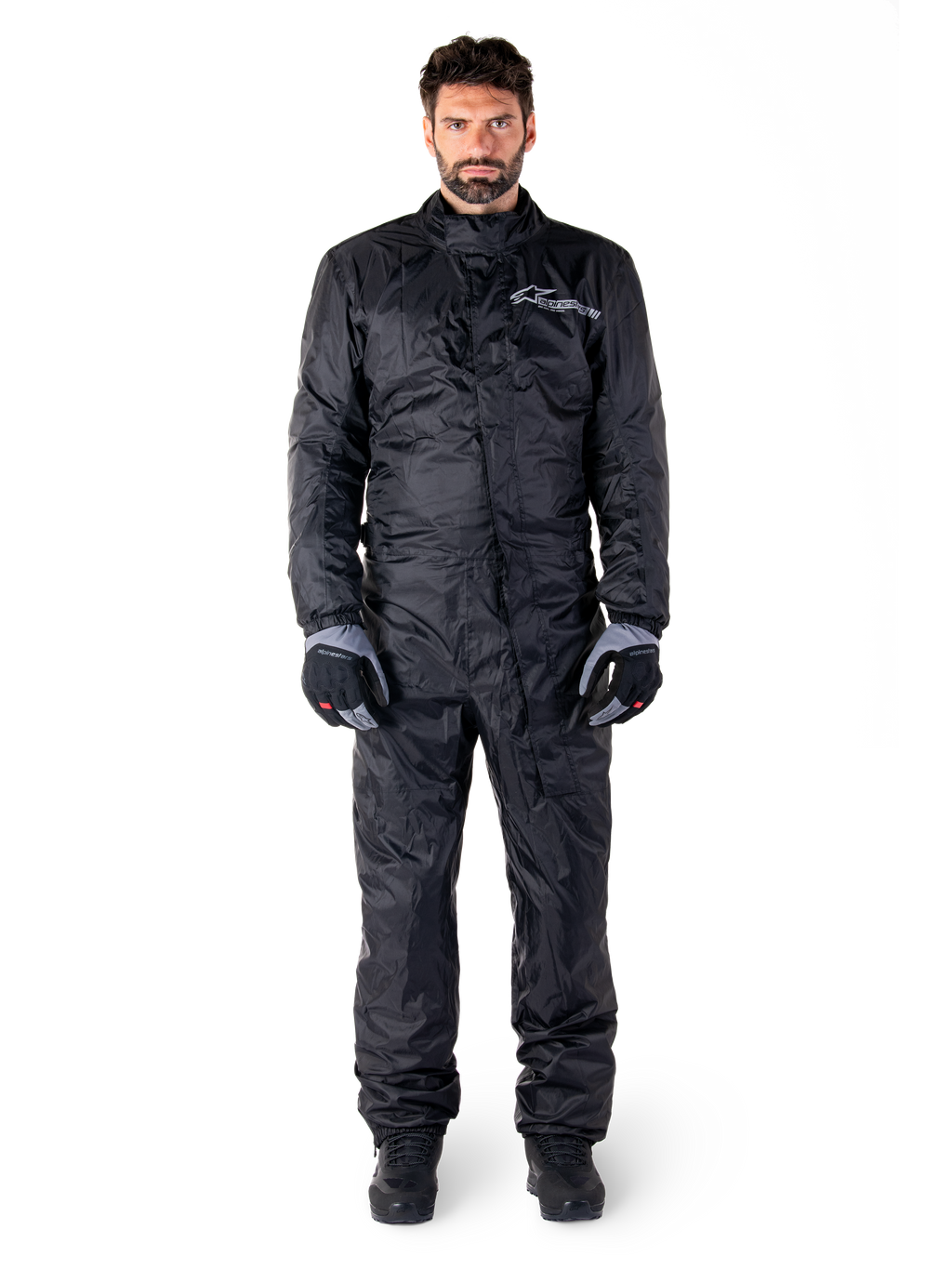Alpinestars Hurricane Rain V2 Suit, traje impermeable de cuerpo completo para moto en negro, equipo de protección impermeable con cuello alto y cierre frontal contra tormentas, con logotipo blanco en el pecho, usado con guantes y botas en negro y gris