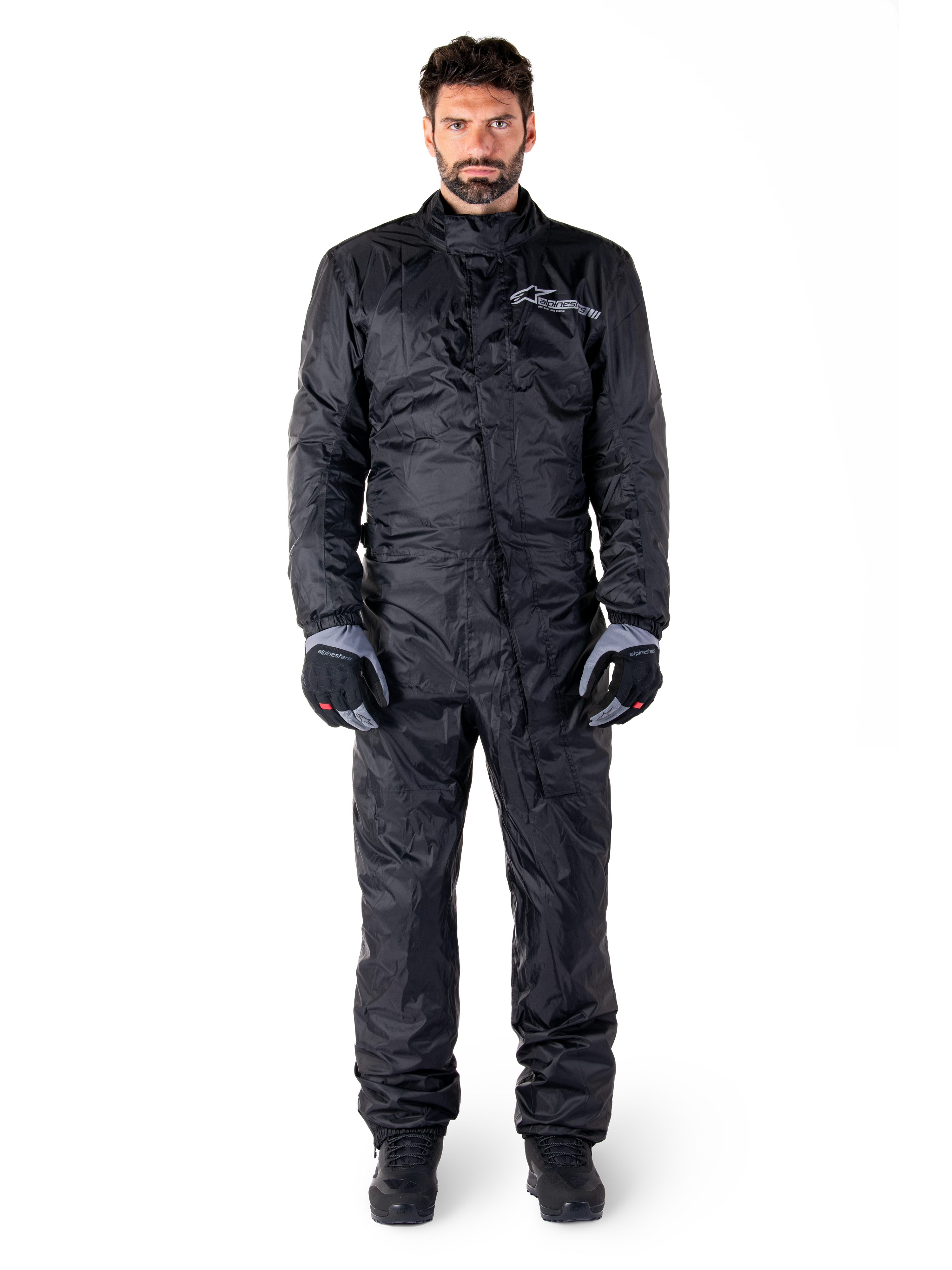 Alpinestars Hurricane Rain V2 Suit, traje impermeable de cuerpo completo para moto en negro, equipo de protección impermeable con cuello alto y cierre frontal contra tormentas, con logotipo blanco en el pecho, usado con guantes y botas en negro y gris