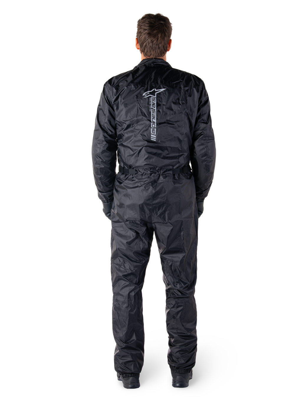 Mono Hurricane Rain V2 de Alpinestars, traje de moto impermeable de una pieza en color negro, vista trasera que muestra el logotipo y la marca denominativa vertical de Alpinestars en grande, tejido ligero arrugado con cintura y puños elásticos, diseñado para la protección al conducir bajo la lluvia.