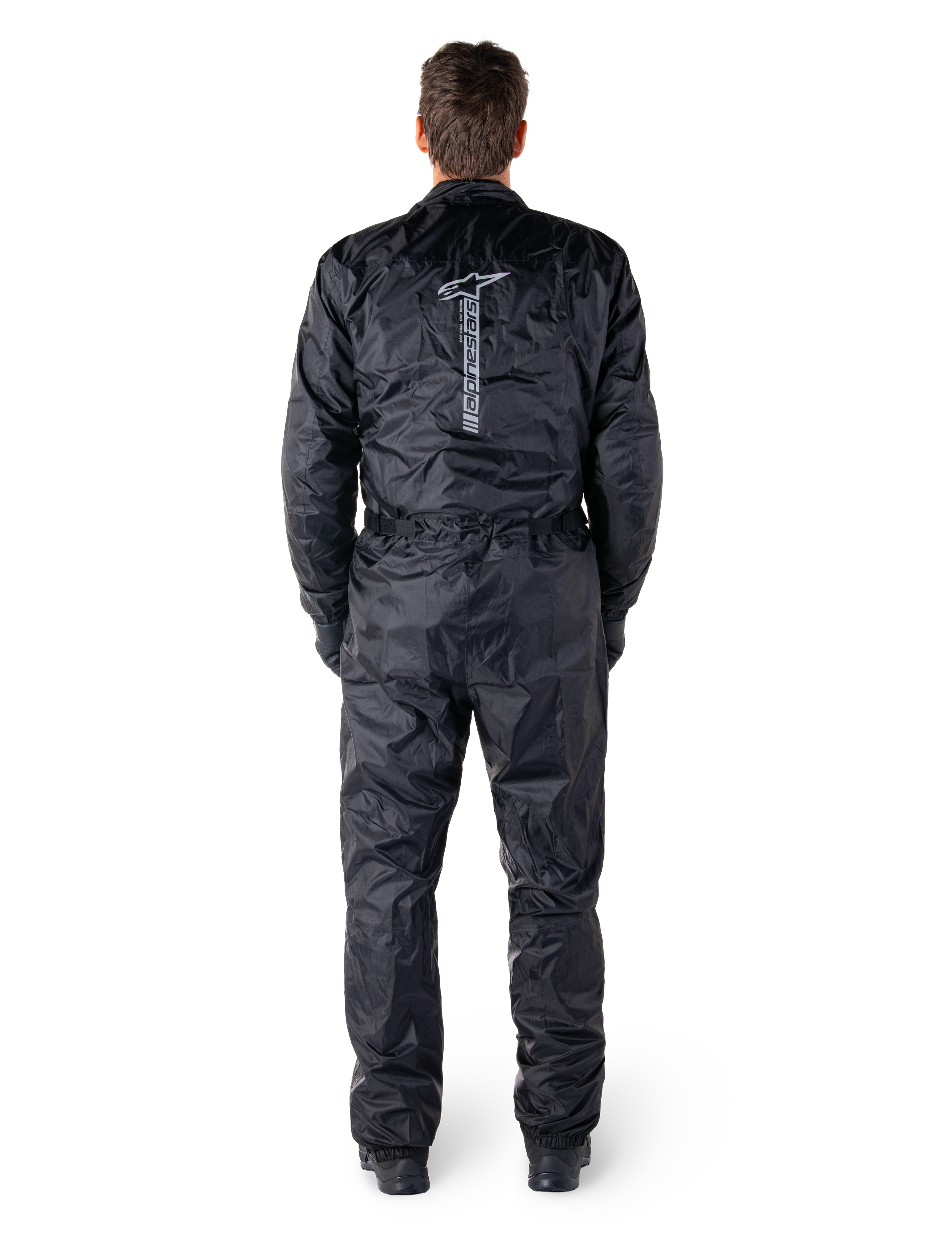 Mono Hurricane Rain V2 de Alpinestars, traje de moto impermeable de una pieza en color negro, vista trasera que muestra el logotipo y la marca denominativa vertical de Alpinestars en grande, tejido ligero arrugado con cintura y puños elásticos, diseñado para la protección al conducir bajo la lluvia.