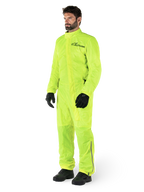 Mono Alpinestars Hurricane Rain V2, traje impermeable de moto de una sola pieza, amarillo flúor, usado con guantes y botas negros, con el logotipo negro de Alpinestars en el pecho y detalles reflectantes en las piernas