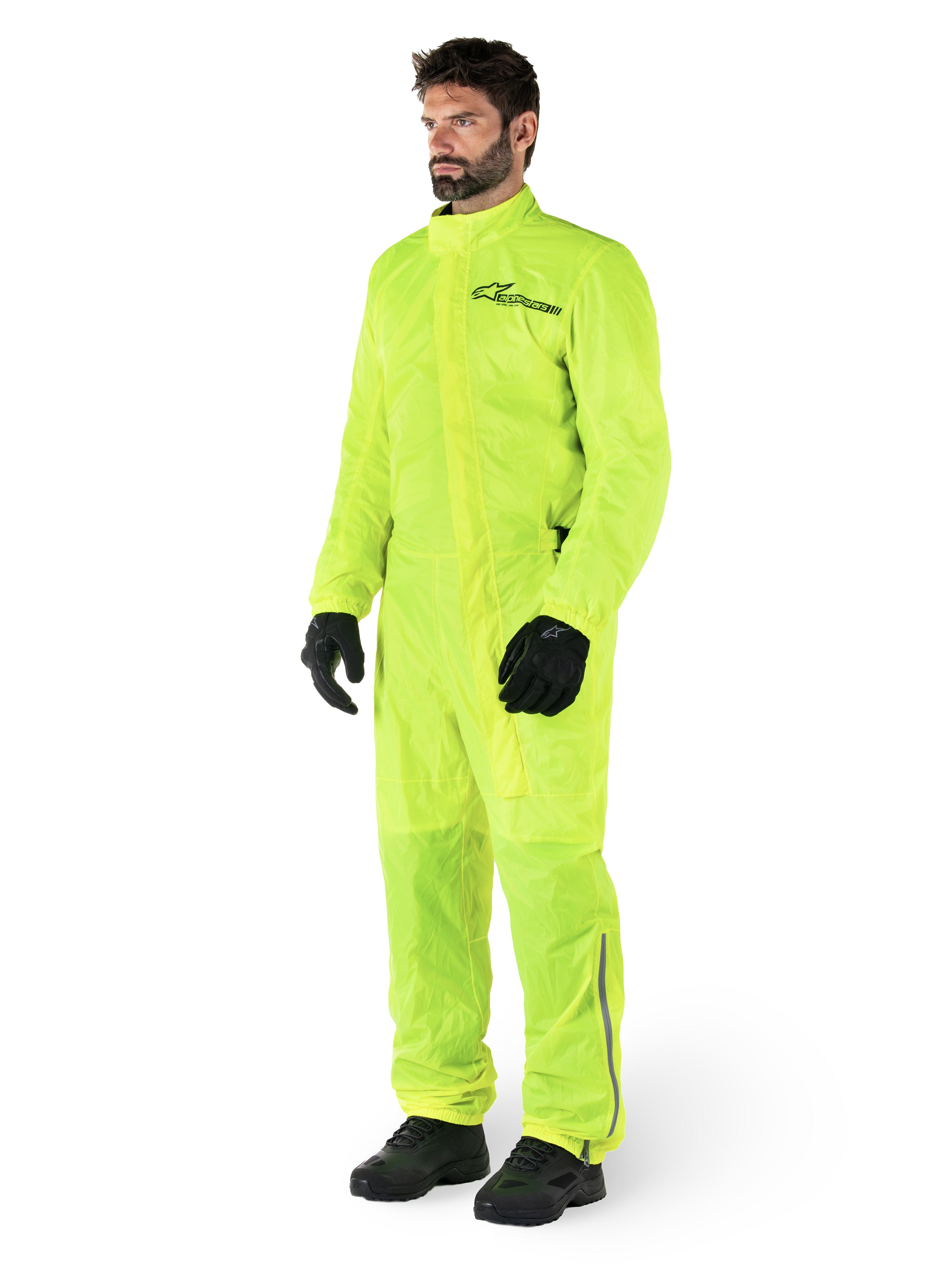 Mono Alpinestars Hurricane Rain V2, traje impermeable de moto de una sola pieza, amarillo flúor, usado con guantes y botas negros, con el logotipo negro de Alpinestars en el pecho y detalles reflectantes en las piernas