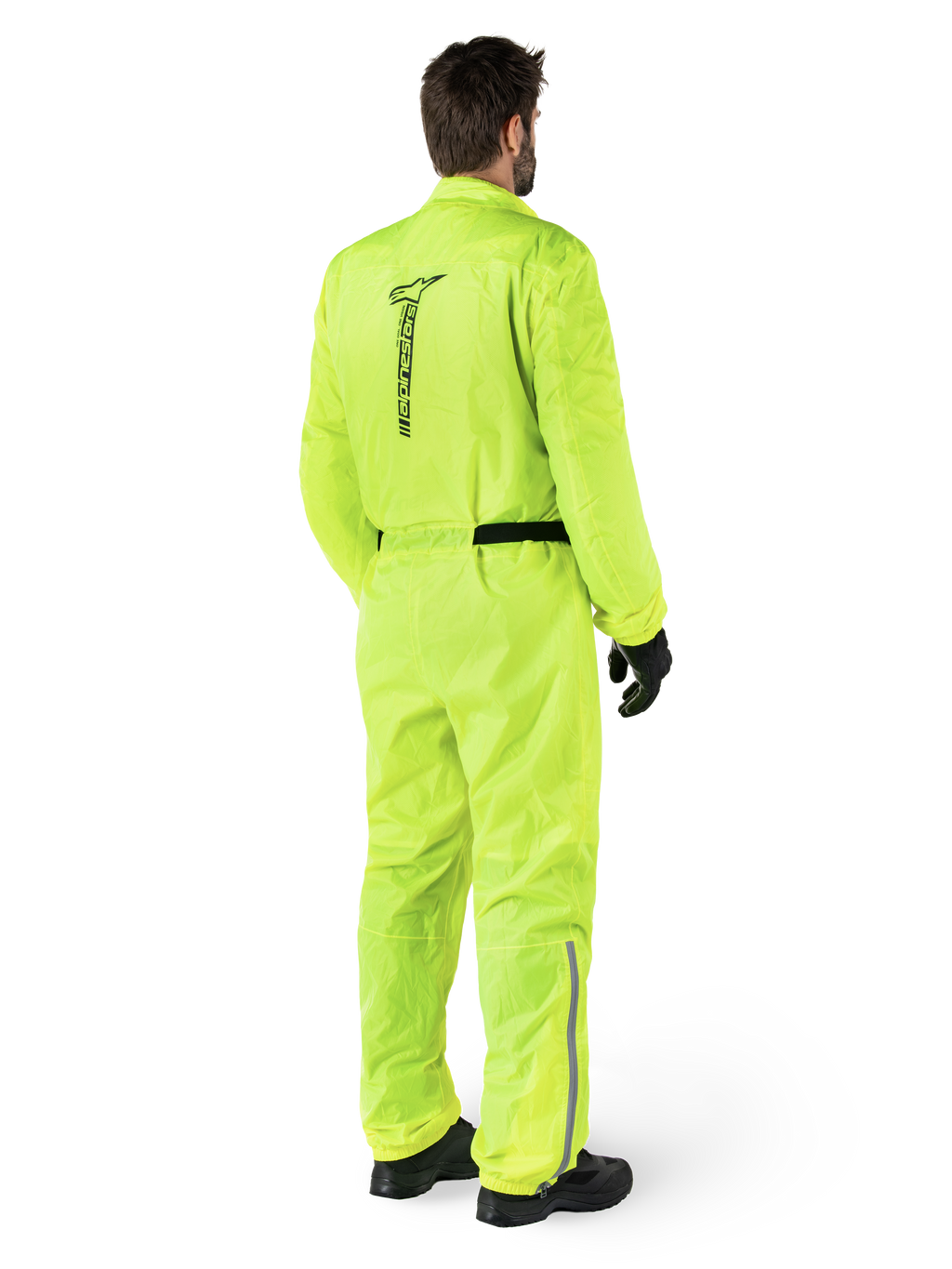 Mono Alpinestars Hurricane Rain V2, Amarillo Flúor, vista trasera de un piloto con un mono impermeable de una pieza para moto, con logotipo negro de Alpinestars en la espalda, cinturón negro y tiras reflectantes en la parte inferior de las piernas, usado con guantes y botas negros