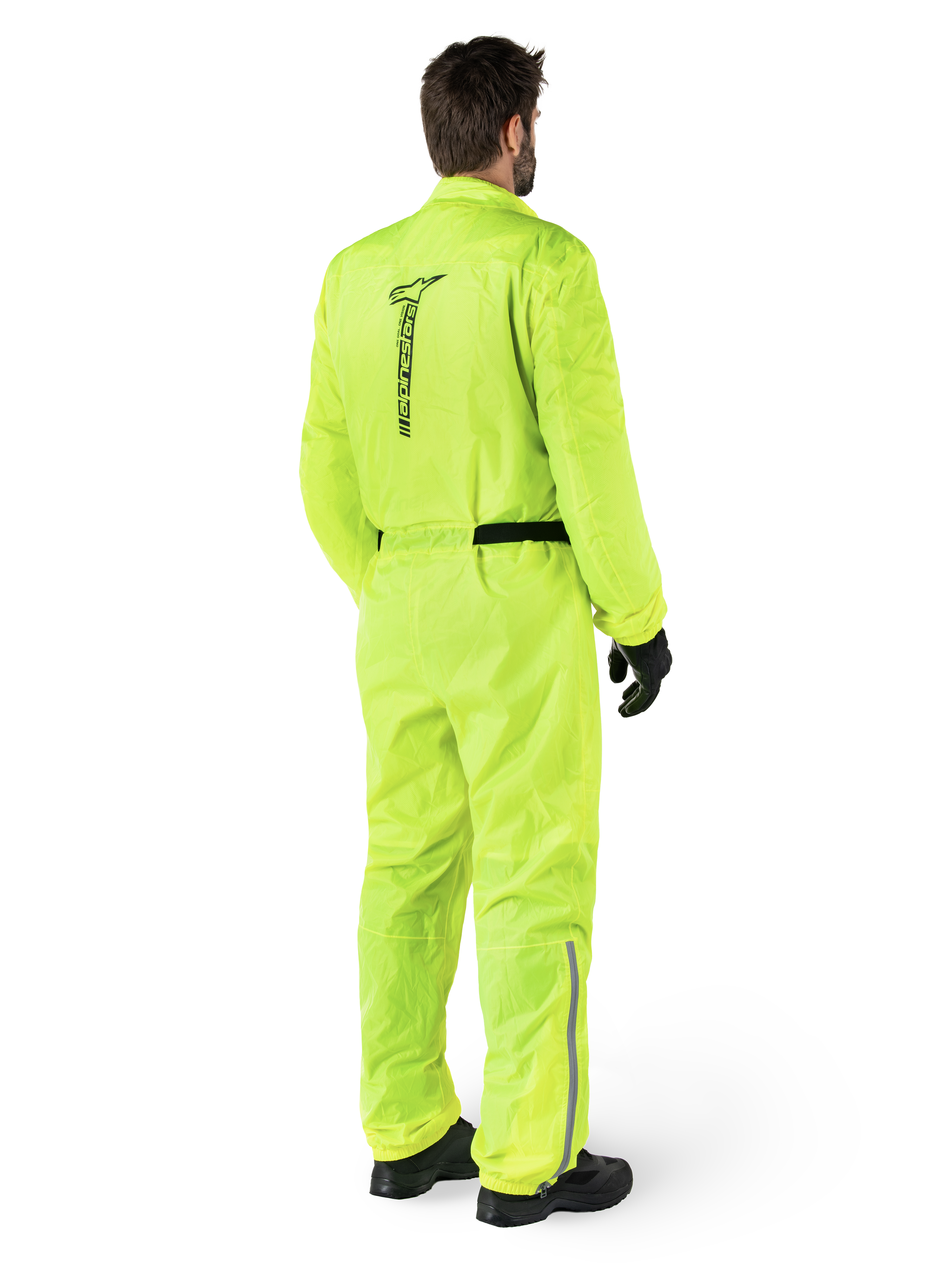 Mono Alpinestars Hurricane Rain V2, Amarillo Flúor, vista trasera de un piloto con un mono impermeable de una pieza para moto, con logotipo negro de Alpinestars en la espalda, cinturón negro y tiras reflectantes en la parte inferior de las piernas, usado con guantes y botas negros