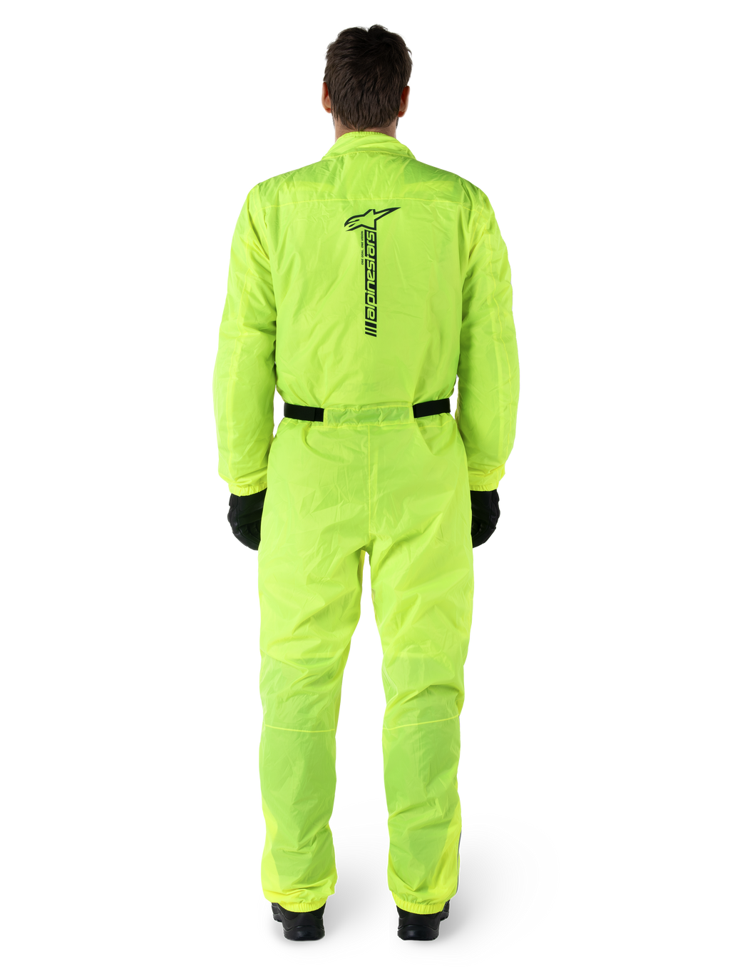 Mono Alpinestars Hurricane Rain V2, traje de lluvia de una pieza para moto, amarillo flúor, vista posterior con marca Alpinestars vertical en negro, cintura y puños elásticos, usado con guantes y botas negras, equipamiento impermeable y resistente al viento