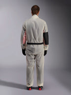 Alpinestars Kart Rain Suit, sobretraje de karting, transparente traslúcido, vista posterior que muestra un panel negro reforzado en el codo derecho para protección contra el calor, cintura elástica con ribete negro, material transparente que deja ver un mono de carreras debajo, combinado con guantes negros y botas de carreras.