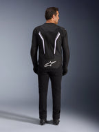 Chaqueta Alpinestars AST V3 Air, vista trasera, negro y gris oscuro con detalles blancos, con un gran logotipo Astar blanco en la parte inferior trasera, franjas reflectantes en la espalda y construcción de tejido de malla, combinada con pantalones y botas negras para un look deportivo