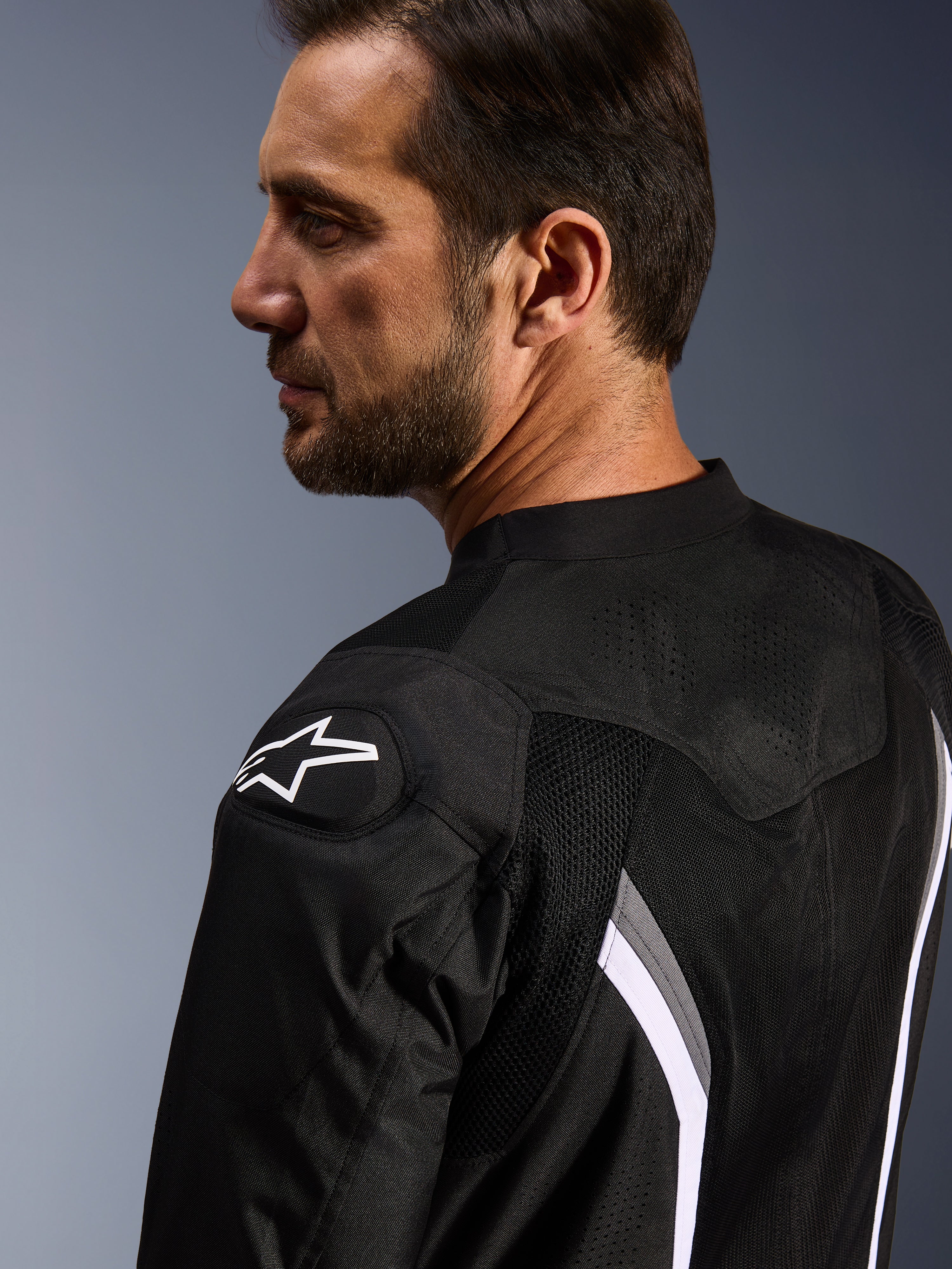 Alpinestars AST V3 Air Jacket, chaqueta de moto, negro, gris oscuro y blanco, vista de cerca desde atrás que muestra el logotipo de la estrella blanca en el hombro y paneles de malla perforados con láser para la ventilación.