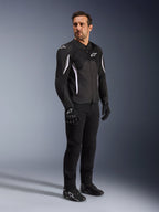 Chaqueta Alpinestars AST V3 Air, negra con detalles y logotipos en blanco, chaqueta ligera de motociclismo con ventilación de malla, usada por un hombre con pantalones, guantes y calzado de moto negros, equipamiento técnico de verano para conducción deportiva y urbana.