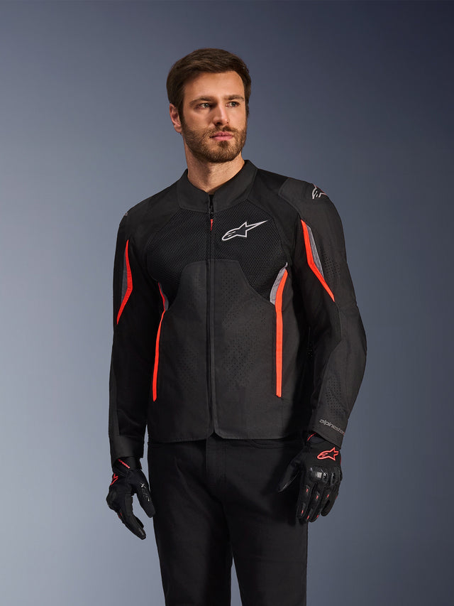 Chaqueta Alpinestars AST V3 Air, negro, gris oscuro y rojo flúor, usada por un hombre con guantes a juego y pantalones negros, con paneles de malla técnica, secciones del pecho perforadas con láser y vibrantes detalles en rojo, ropa de alto rendimiento para motociclismo deportivo
