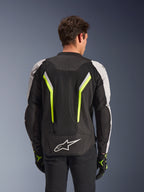 Chaqueta Alpinestars AST V3 Air, Negro Plata Amarillo Fluo, vista trasera en modelo, chaqueta textil para moto con paneles de ventilación de malla dual tech, franjas verticales en amarillo neón, mangas plateadas y logotipo blanco de Alpinestars en la parte inferior de la espalda.