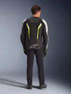 Chaqueta Alpinestars AST V3 Air, chaqueta textil de moto, negro, plata y amarillo flúor, vista trasera que muestra los paneles de ventilación de malla y detalles fluorescentes, usada con pantalones negros y guantes de moto, equipamiento deportivo de alto rendimiento