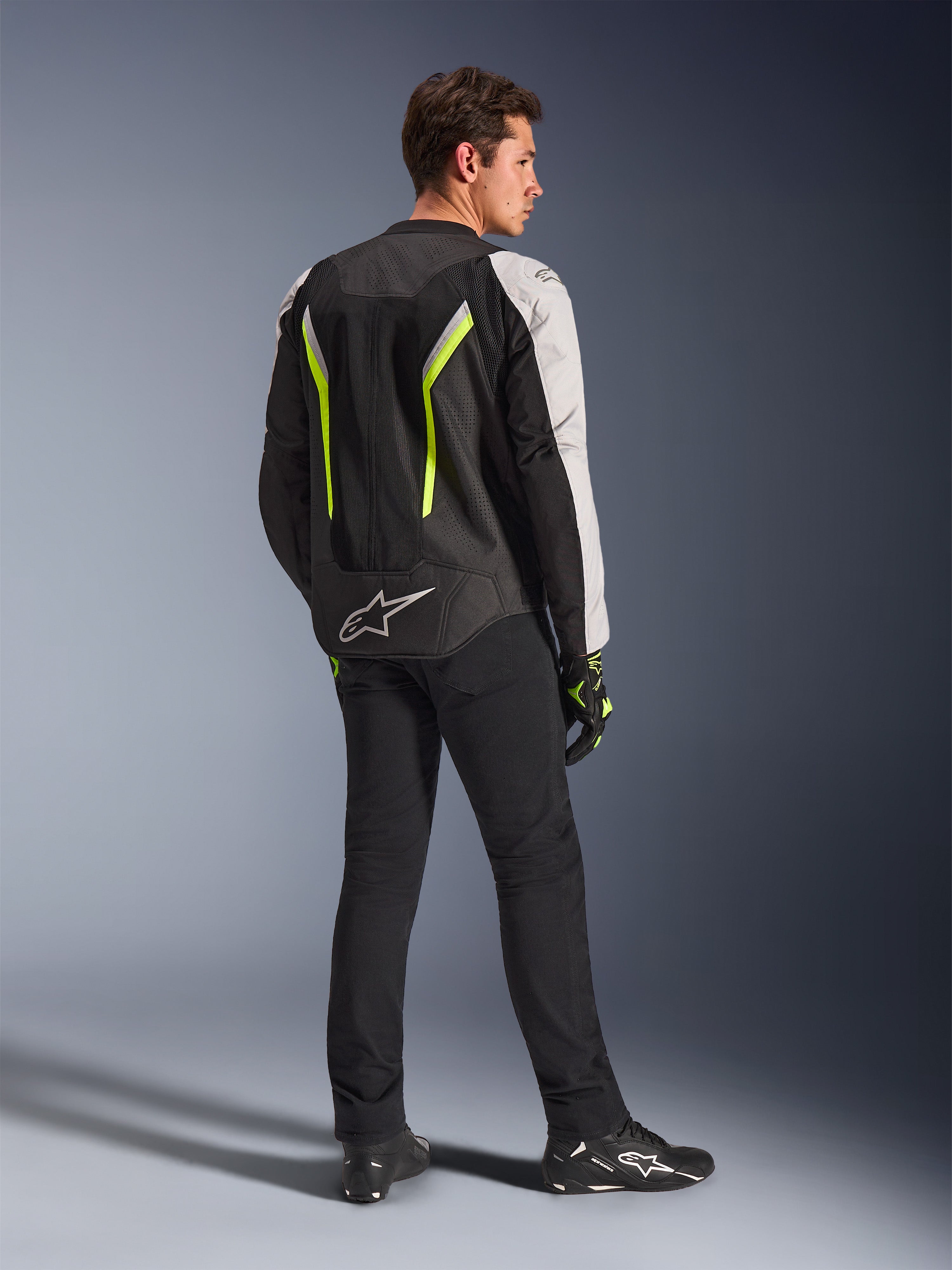 Alpinestars AST V3 Air Jacket en Negro Plata Amarillo Flúor, chaqueta textil de motociclismo para hombre vista desde atrás, con amplios paneles de malla y detalles en amarillo flúor, combinada con pantalones, guantes y calzado Alpinestars en color negro, equipamiento técnico para conducción deportiva.