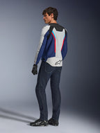 Chaqueta Alpinestars AST V3 Air, chaqueta de moto en plateado, azul profundo y rojo brillante, vista posterior combinada con vaqueros de moto azul oscuro y equipamiento negro, con paneles de malla transpirable y el logotipo de Alpinestars en la espalda, equipamiento técnico de ajuste deportivo.