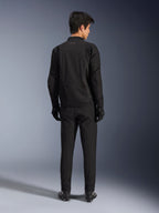 Chaqueta Alpinestars Aeroshell Airflow en Black Anthracite, vista posterior de un modelo masculino con equipamiento completo de motociclismo, pantalones y guantes negros, con construcción ligera de softshell y parte trasera alargada para mayor cobertura.
